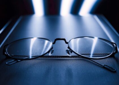 A pair of eyeglasses rests on a glowing screen, illustrating the comparison of blue light glasses and screen filters.