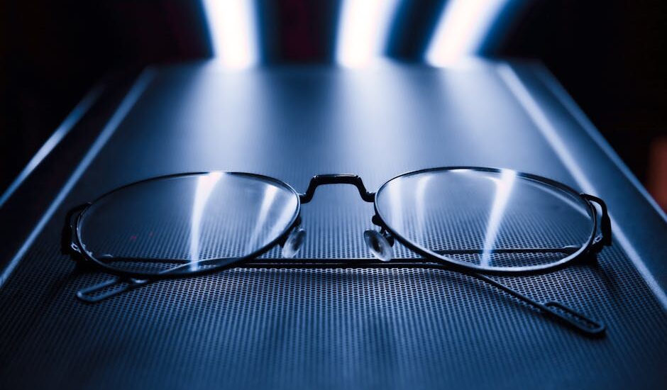 A pair of eyeglasses rests on a glowing screen, illustrating the comparison of blue light glasses and screen filters.