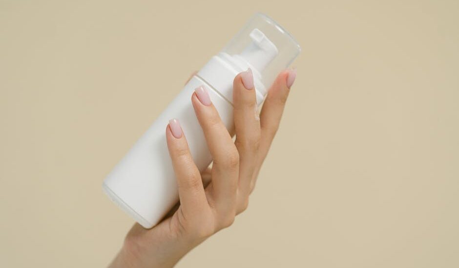 A close-up of a hand holding a white cosmetic bottle against a neutral background, perfect for product mockups and beauty industry use.