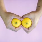 Hands holding two lemons side by side on a pink surface, visually referencing the breast pump vs hand expressing topic