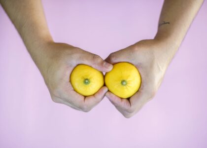 Hands holding two lemons side by side on a pink surface, visually referencing the breast pump vs hand expressing topic