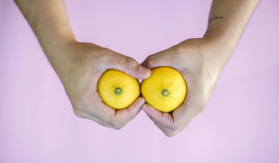 Hands holding two lemons side by side on a pink surface, visually referencing the breast pump vs hand expressing topic