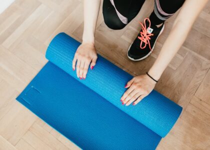 From above of unrecognizable female athlete in leggings and sneakers unfolding sport mat for practicing yoga in morning at home
