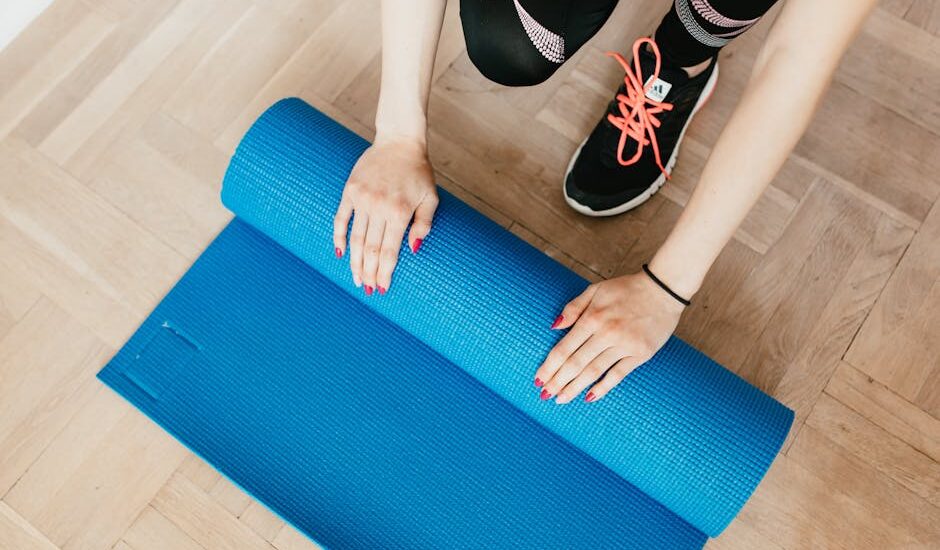 From above of unrecognizable female athlete in leggings and sneakers unfolding sport mat for practicing yoga in morning at home