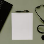 Medical workspace featuring a blank paper, stethoscope, and laptop from above.