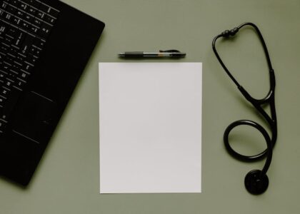Medical workspace featuring a blank paper, stethoscope, and laptop from above.