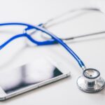 A blue stethoscope and a smartphone on a white surface, illustrating the digital vs analog stethoscope discussion.