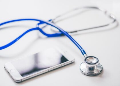 A blue stethoscope and a smartphone on a white surface, illustrating the digital vs analog stethoscope discussion.