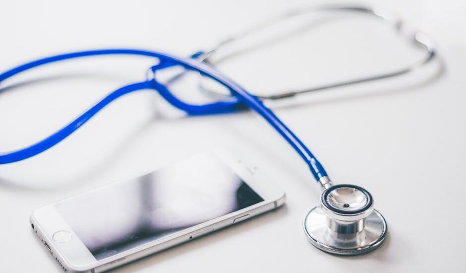 A blue stethoscope and a smartphone on a white surface, illustrating the digital vs analog stethoscope discussion.