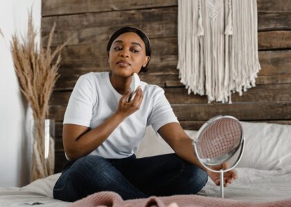 A woman sits on a bed using an electric facial massager, illustrating self-care practices related to electric eye massager benefits.