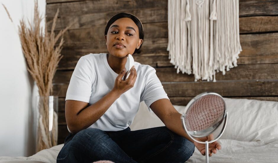 A woman sits on a bed using an electric facial massager, illustrating self-care practices related to electric eye massager benefits.