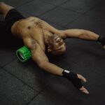 Man stretching on a gym mat with a green electric foam roller under his back, illustrating electric foam roller use.