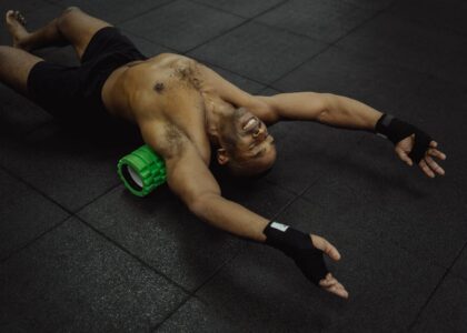 Man stretching on a gym mat with a green electric foam roller under his back, illustrating electric foam roller use.