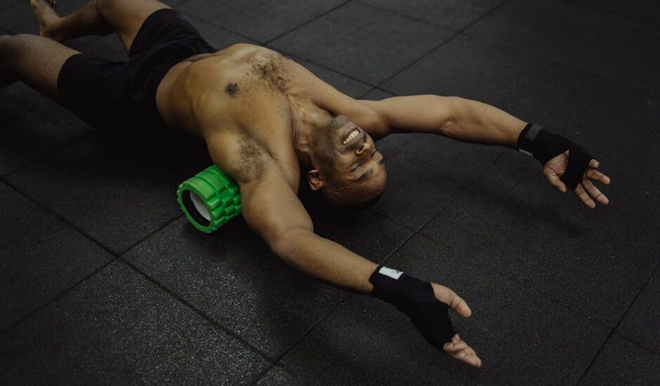 Man stretching on a gym mat with a green electric foam roller under his back, illustrating electric foam roller use.