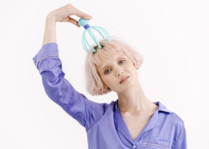 Person in a purple shirt using an electric scalp massager on their head, illustrating electric scalp massager use for the article topic.