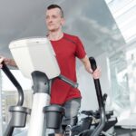 Man with a prosthetic leg working out on an elliptical trainer in a bright, modern gym.