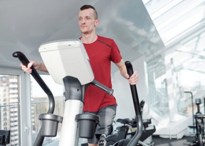 Man with a prosthetic leg working out on an elliptical trainer in a bright, modern gym.