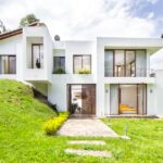 A contemporary white house surrounded by lush greenery on a hillside, showcasing modern architecture.