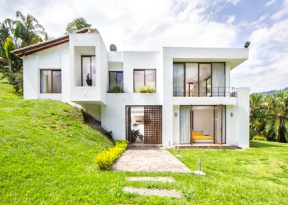 A contemporary white house surrounded by lush greenery on a hillside, showcasing modern architecture.