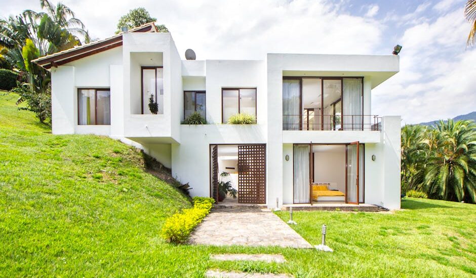 A contemporary white house surrounded by lush greenery on a hillside, showcasing modern architecture.