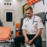 A paramedic takes a moment to rest inside an ambulance, seated with eyes closed.
