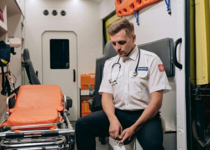 A paramedic takes a moment to rest inside an ambulance, seated with eyes closed.