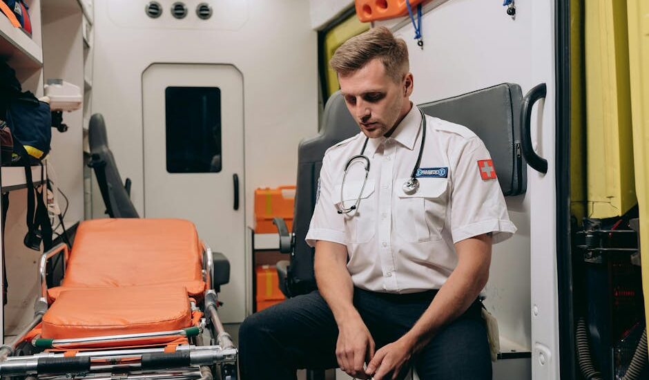 A paramedic takes a moment to rest inside an ambulance, seated with eyes closed.