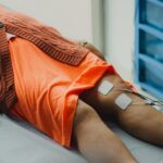 Person lying on a medical table with electrode pads attached to their thighs, illustrating EMS and TENS pain relief methods.