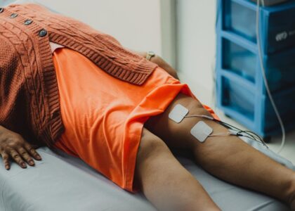 Person lying on a medical table with electrode pads attached to their thighs, illustrating EMS and TENS pain relief methods.