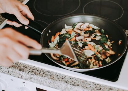 A person stirring vibrant vegetables in a frying pan on an electric stove.