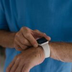 Older adult in a blue shirt interacts with a white wrist-worn GPS medical alert bracelet, highlighting senior safety tech.