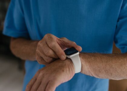 Older adult in a blue shirt interacts with a white wrist-worn GPS medical alert bracelet, highlighting senior safety tech.