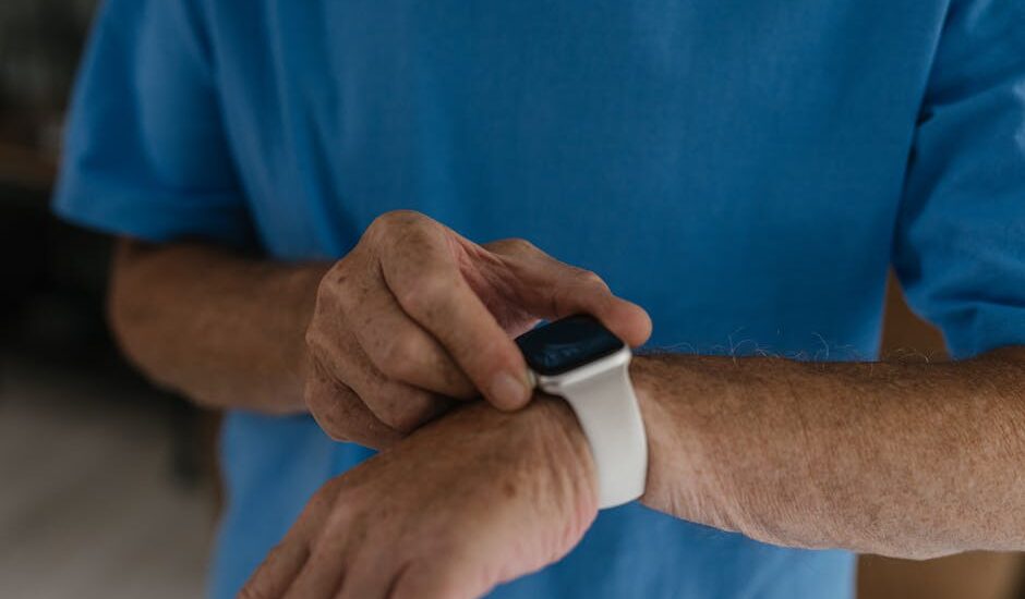 Older adult in a blue shirt interacts with a white wrist-worn GPS medical alert bracelet, highlighting senior safety tech.