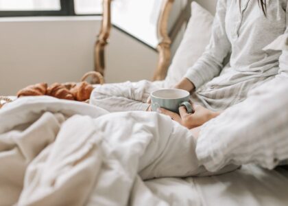 A relaxing morning scene with a woman enjoying coffee in bed with warm blankets and croissants.