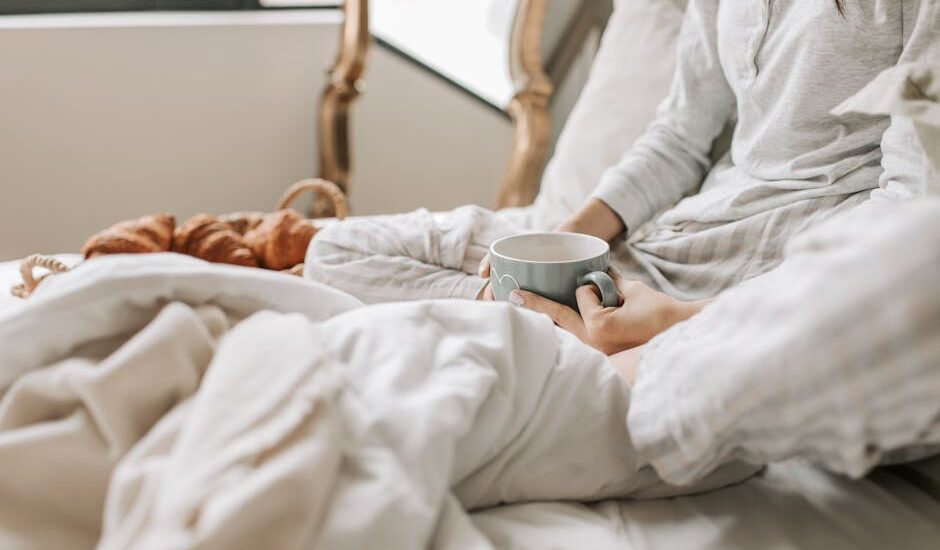 A relaxing morning scene with a woman enjoying coffee in bed with warm blankets and croissants.
