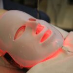 Person using a red light therapy mask, illustrating how these devices work for skin treatment in the article topic.