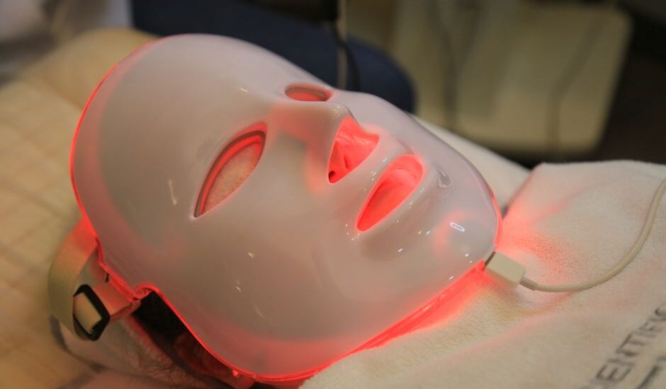 Person using a red light therapy mask, illustrating how these devices work for skin treatment in the article topic.