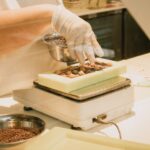Chef in gloves arranging chocolate and ingredients on a kitchen scale for confectionery preparation.