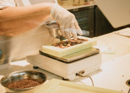 Chef in gloves arranging chocolate and ingredients on a kitchen scale for confectionery preparation.