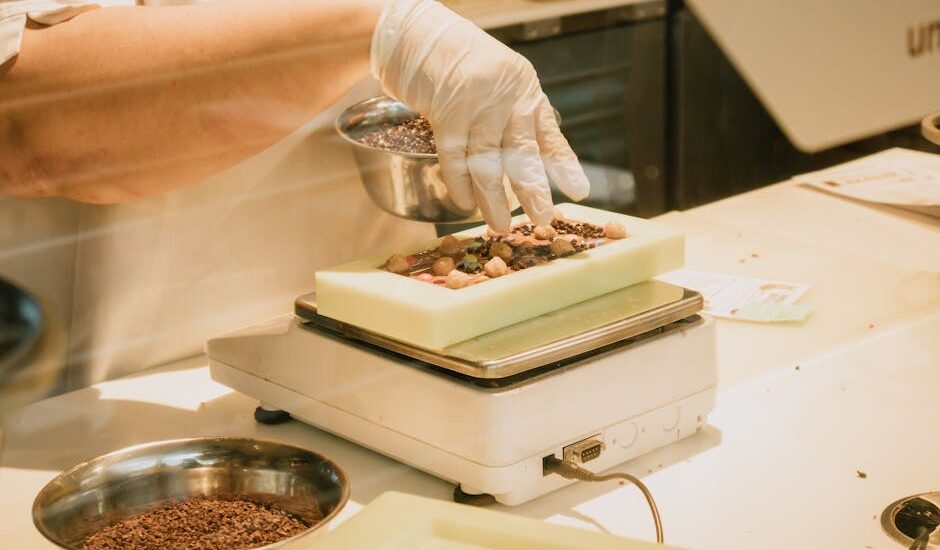 Chef in gloves arranging chocolate and ingredients on a kitchen scale for confectionery preparation.