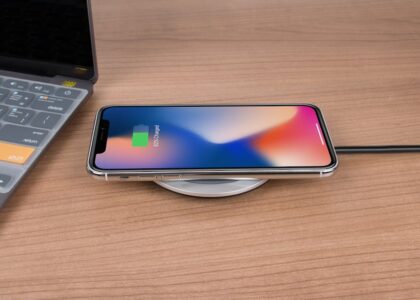 A smartphone charging wirelessly on a round charging pad next to a laptop, illustrating charging technology for the electric heating pad guide.