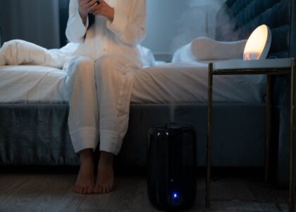 A person in pajamas sits on a bed near a running humidifier, illustrating how to choose a humidifier for bedroom comfort.