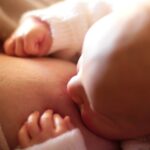 Intimate close-up of a newborn baby breastfeeding, captured in warm, softly lit setting.