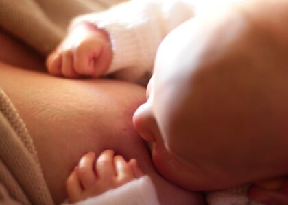 Intimate close-up of a newborn baby breastfeeding, captured in warm, softly lit setting.