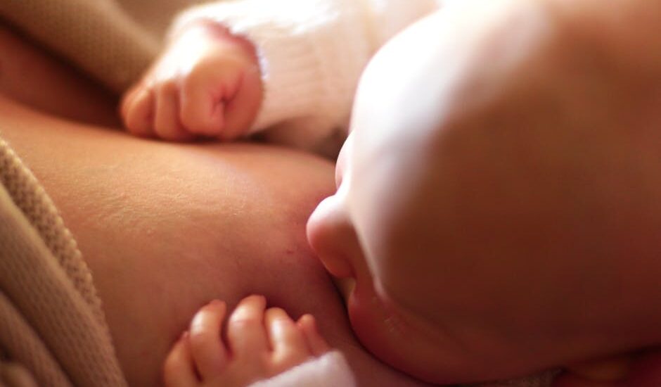 Intimate close-up of a newborn baby breastfeeding, captured in warm, softly lit setting.