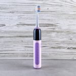 A purple and black electric toothbrush stands upright on a gray surface, illustrating electric toothbrush options for buyers.