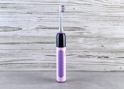 A purple and black electric toothbrush stands upright on a gray surface, illustrating electric toothbrush options for buyers.