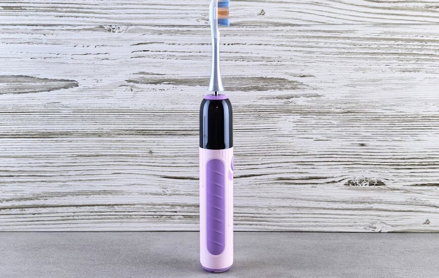 A purple and black electric toothbrush stands upright on a gray surface, illustrating electric toothbrush options for buyers.