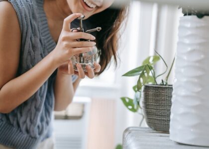 A woman smiling while using a spray bottle to water indoor plants in a cozy room.