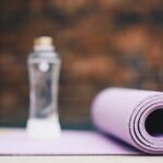 A rolled purple fitness mat and a clear spray bottle, illustrating cleaning tips for maintaining a germ-free workout space